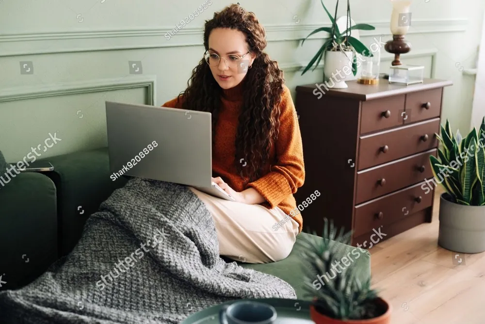 A woman relaxing on her sofa at home with a laptop and a cup of tea