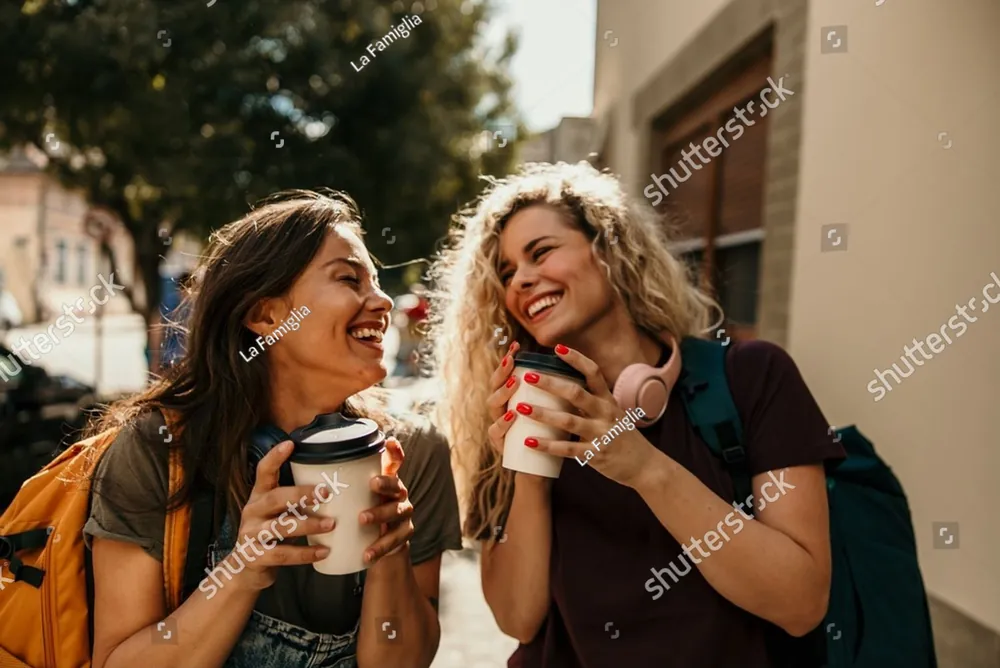 Two friends laughing together over coffee on a city street