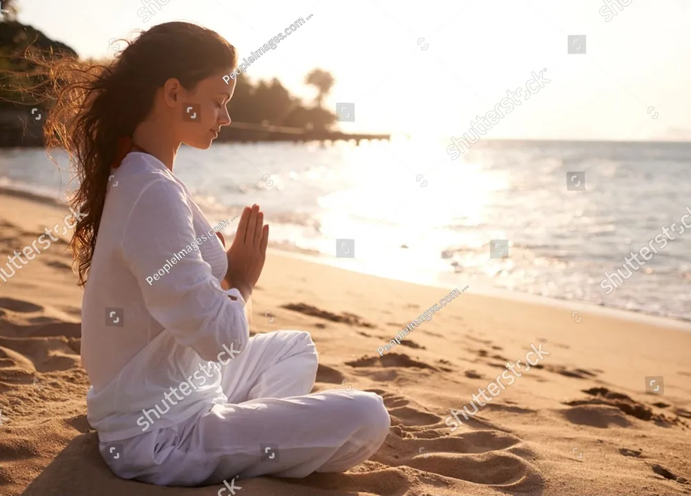 A woman meditating on the beach at sunset