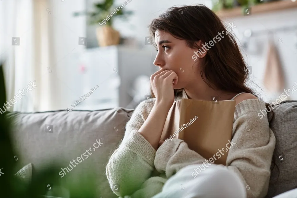 A young woman sitting on her sofa, lost in thought
