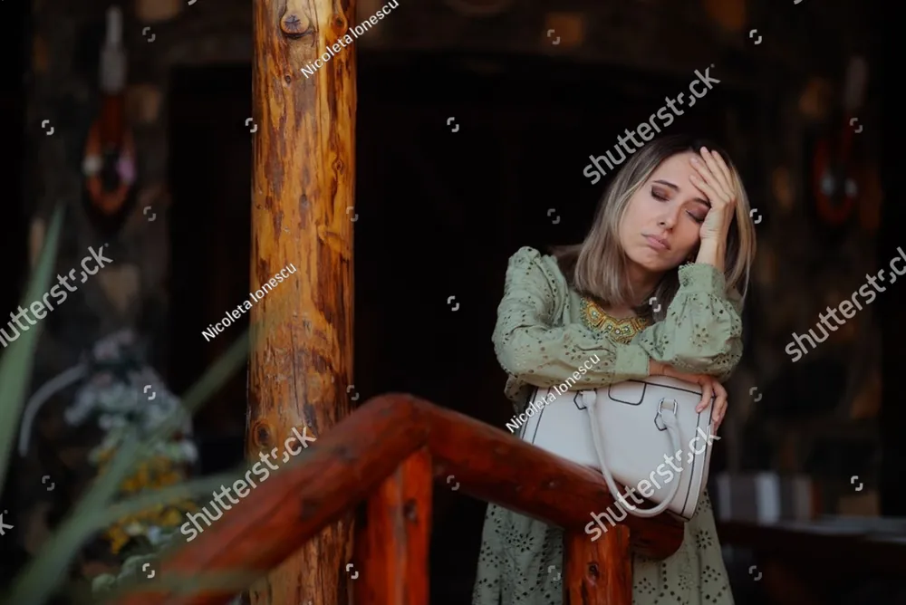 A tired woman leaning on a porch railing, holding her head