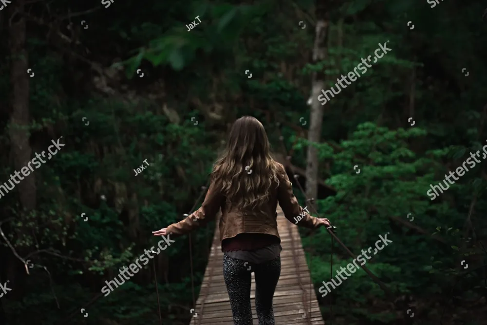 A woman walking a wooden boardwalk through the forest, arms open