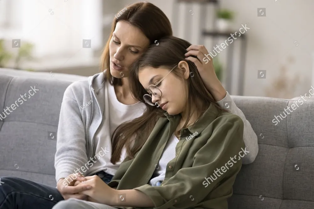 A mother comforting her teenage daughter on the sofa