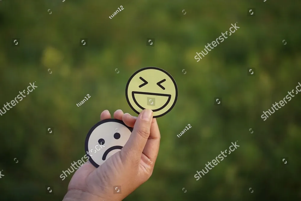 A hand holding a laughing face over a sad face
