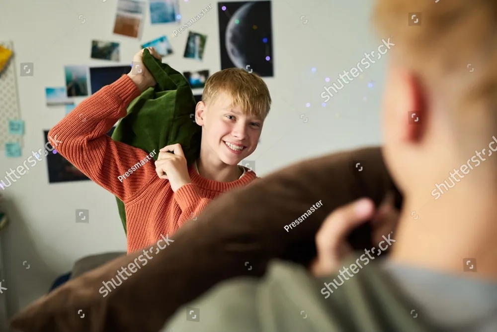 A smiling teenage boy being playfully hit with a pillow at home