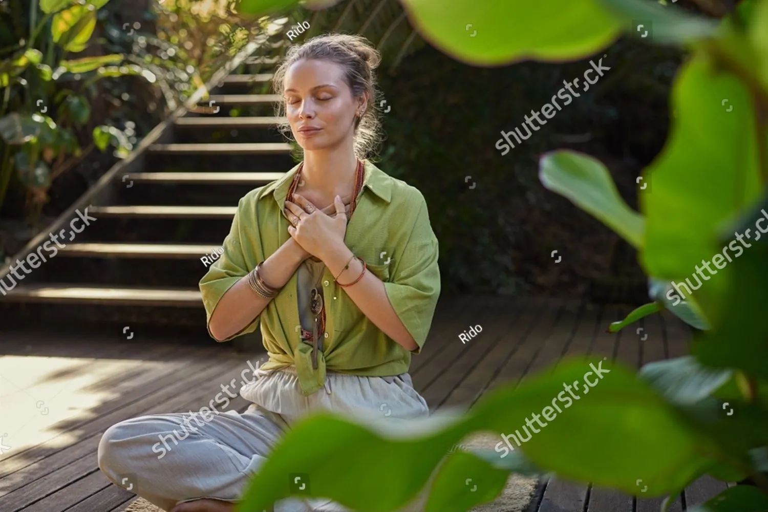 A woman meditating with her hands on her heart in a garden